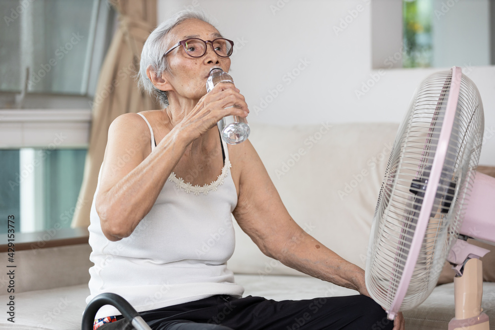 Old elderly woman drinking a bottle of water,keeping body water  balance,drink a lot of water to prevent dehydration in heat hot summer  weather while stay at home,prevention of heat stroke,health care. Stock