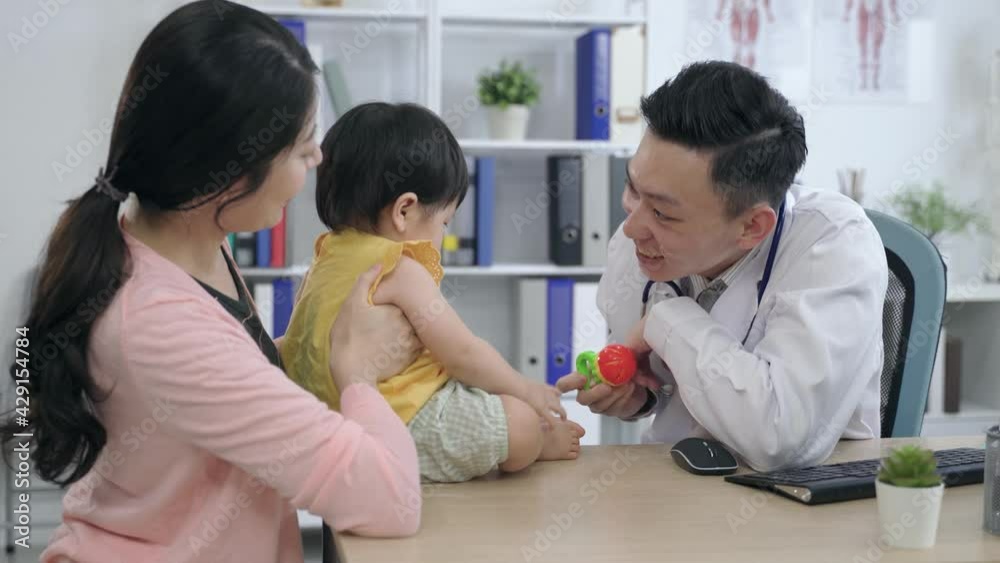 friendly male physician is playing with the child patient by not letting her touch the handheld rattle on purpose during a routine visit in his office friendly male physician is playing with the child patient by not letting her touch the handheld rattle on purpose during a routine visit in his office