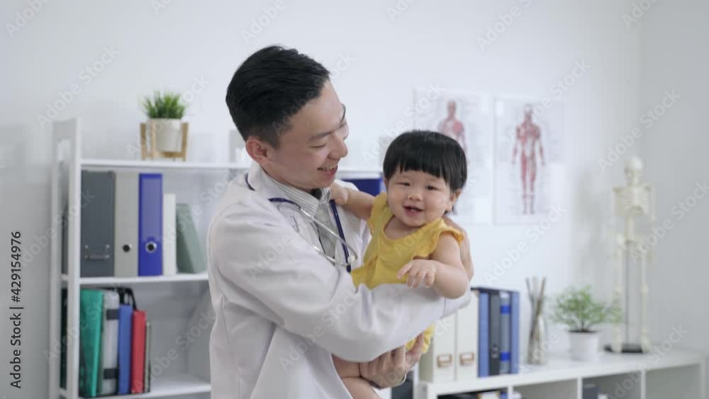 little girl is laughing happily while looking at the camera and pointing into distance with curiosity in the pediatrician’s arms at a clinic office. little girl is laughing happily while looking at the camera and pointing into distance with curiosity in the pediatrician’s arms at a clinic office.