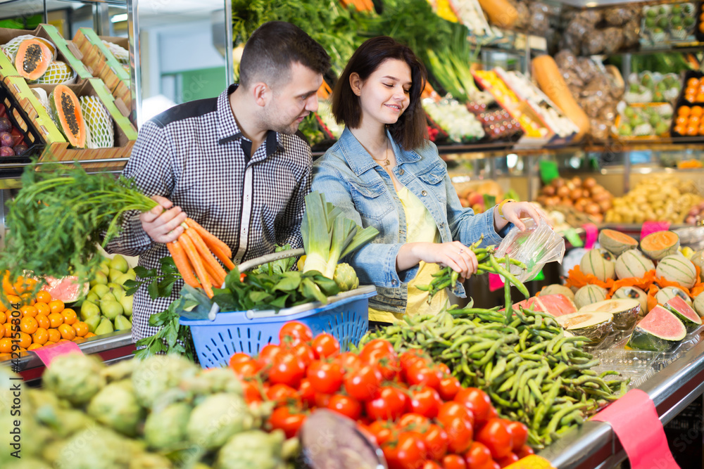 Ordinary couple examining various vegetables in grocery shop