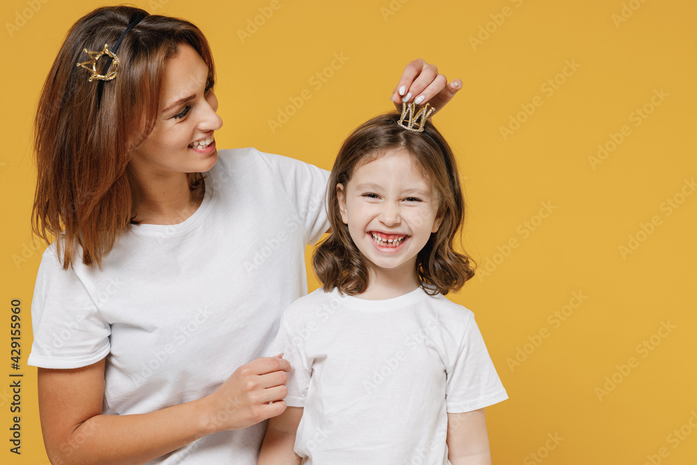Happy woman in basic white t-shirt diadem have fun with cute child baby girl 5-6 years old Mom little princess kid daughter isolated on yellow color background studio Mother's Day love family concept Happy woman in basic white t-shirt diadem have fun with cute child baby girl 5-6 years old Mom little princess kid daughter isolated on yellow color background studio Mother's Day love family concept