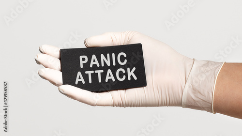 Closeup of the hand in a white sterile glove holding a card with text - PANIC ATTACK