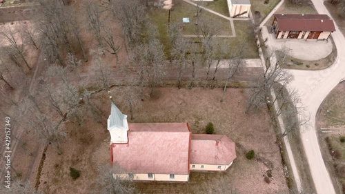 Small village church with golden weather vane cockerel on top of bell tower in Umurga, Latvia. Early spring time. Aerial view from drone.