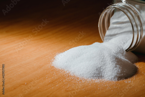 Fotografie Salt spilling from glass jar on  wooden table
