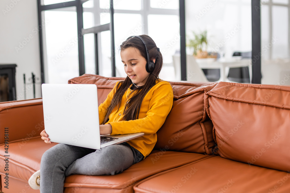 Smart Little Girl Does Homework in Her Living Room. She's Sitting and Uses Laptop. Smart Little Girl Does Homework in Her Living Room. She's Sitting and Uses Laptop.