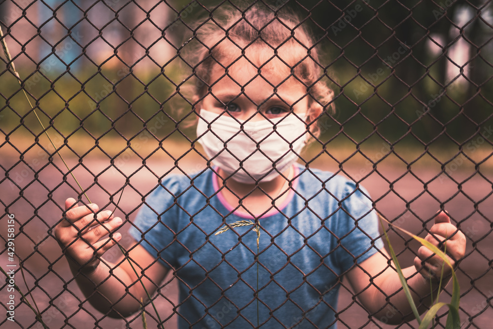 A child in a medical mask holds the fence with his hands A child in a medical mask holds the fence with his hands