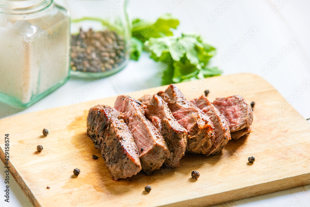 Grilled beef filet Mignon steak or tenderloin on wooden board with pepper, salt and coriander leaves Grilled beef filet Mignon steak or tenderloin on wooden board with pepper, salt and coriander leaves