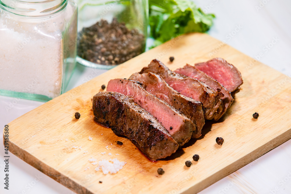 Grilled beef filet Mignon steak or tenderloin on wooden board with pepper, salt and coriander leaves Grilled beef filet Mignon steak or tenderloin on wooden board with pepper, salt and coriander leaves