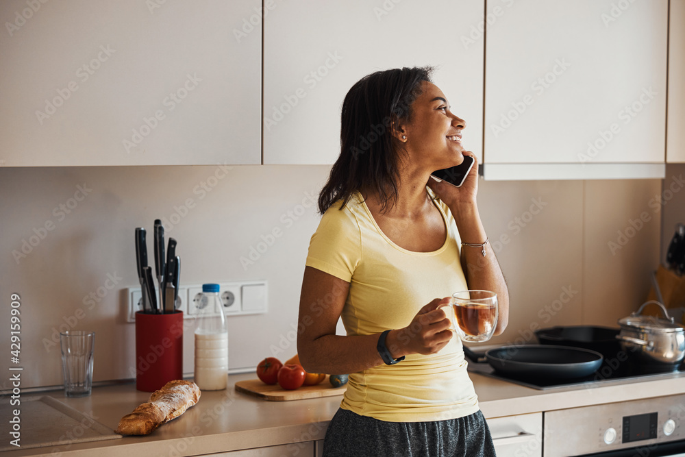 Beautiful young woman talking on cellphone in kitchen Beautiful young woman talking on cellphone in kitchen