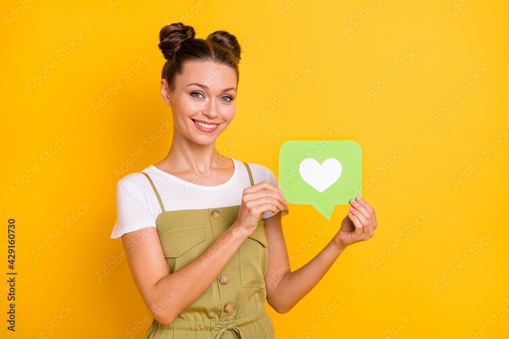 Portrait of attractive cheerful girl holding in hand paper card heart like review isolated over bright yellow color background Portrait of attractive cheerful girl holding in hand paper card heart like review isolated over bright yellow color background