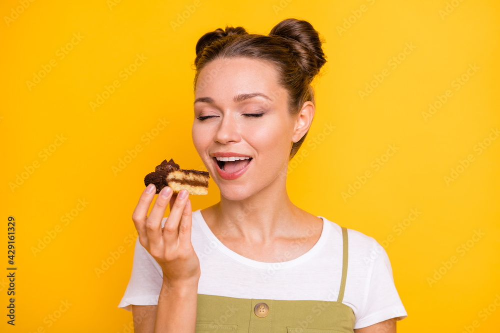 Portrait of attractive dreamy cheerful girl biting piece of cake delicious confectionery isolated over bright yellow color background Portrait of attractive dreamy cheerful girl biting piece of cake delicious confectionery isolated over bright yellow color background