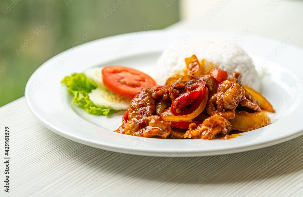 Stir-fried pork with traditional Thai Chili Paste or Moo Pad Prickpow in Thailand language with white jasmine rice, natural light from the window.