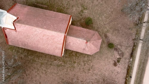 Small village church with golden weather vane cockerel on top of bell tower in Umurga, Latvia. Early spring time. Aerial view from drone.