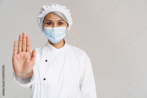 Asian mature woman in chef uniform and face mask gesturing stop sign