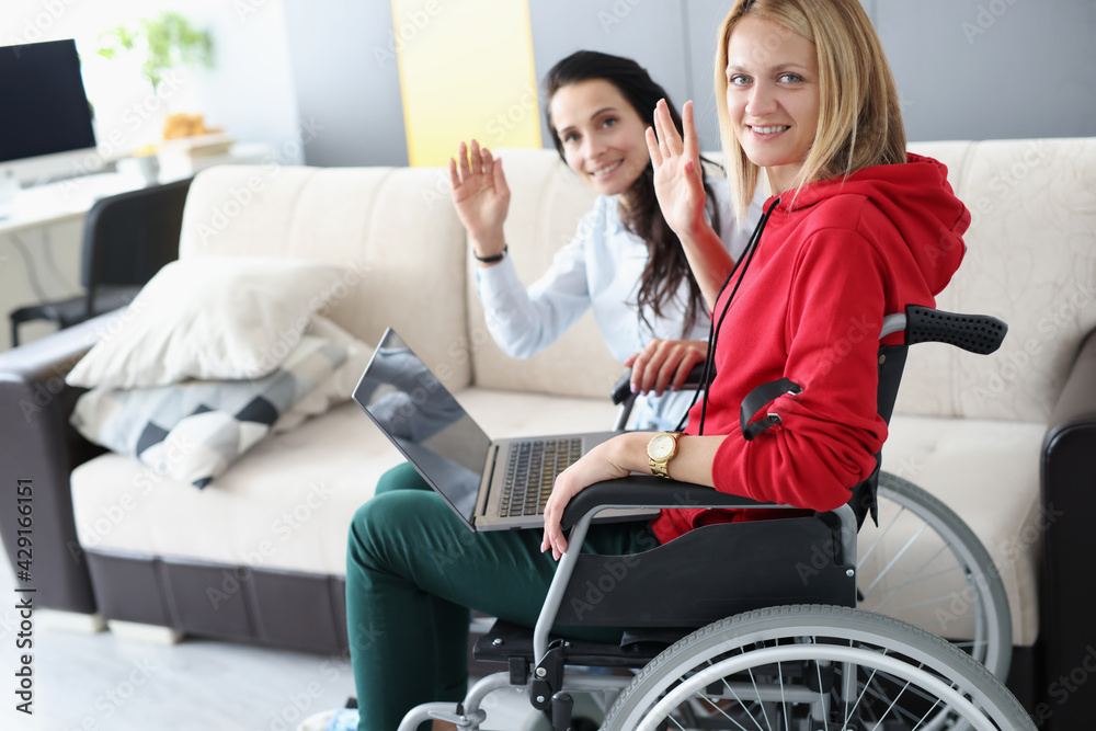 Disabled woman and friend are sitting at laptop and waving at home Disabled woman and friend are sitting at laptop and waving at home