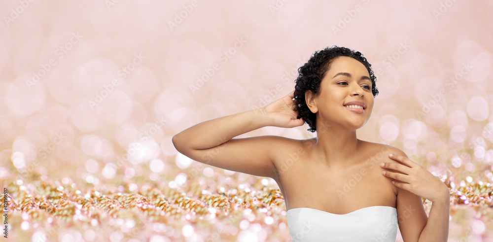 beauty and people concept - portrait of happy smiling young african american woman with bare shoulders touching her hair over pink glitter background beauty and people concept - portrait of happy smiling young african american woman with bare shoulders touching her hair over pink glitter background