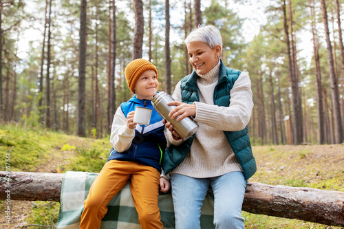 picking season, leisure and people concept - grandmother and grandson having picnic and drinking tea in autumn forest