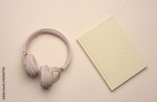 beige wireless headphones and a closed notepad on a beige background