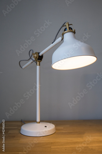 closeup of a lit white table lamp on a wooden table
