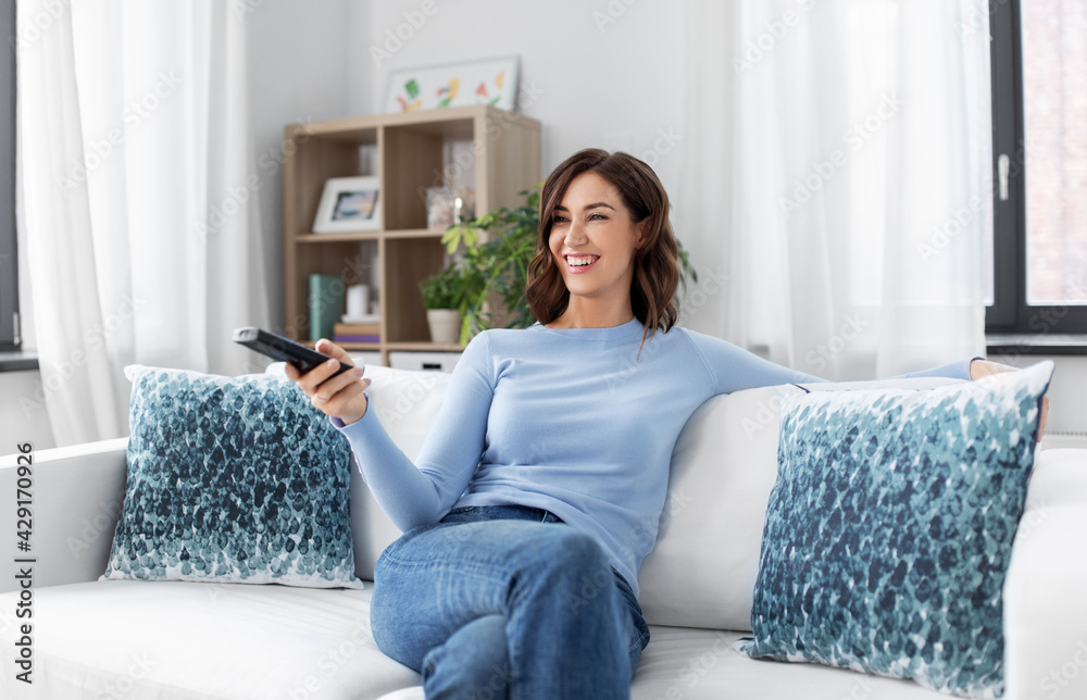 people and leisure concept - happy smiling young woman with remote control watching tv at home people and leisure concept - happy smiling young woman with remote control watching tv at home