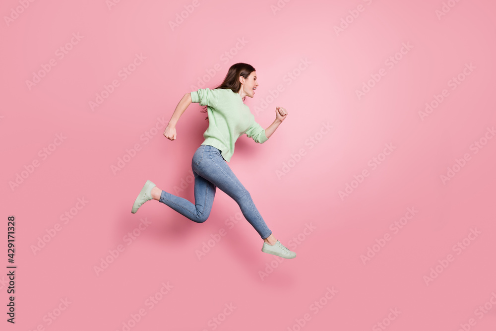 Full size profile photo of brunette nice girl jump run yell wear lime sweater jeans sneakers isolated on pink color background