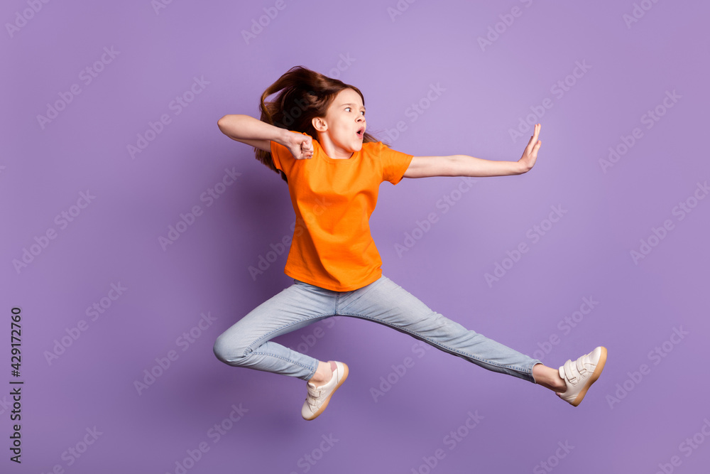 Full body profile photo of optimstic ginger hair girl jump wear orange t-shirt jeans isolated on purple background
