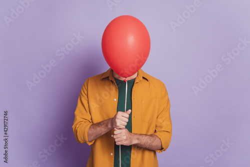 Photo of shy guest guy hold red balloon hide face wear shirt posing on violet background photo