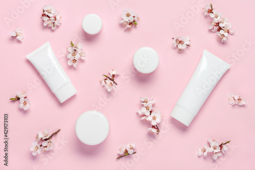 Flat lay composition with cosmetic products and spring flowers on pink background. Pattern