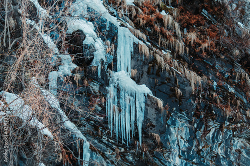 Large frozen icicles on a small waterfall at Solang valley in Manali, Himachal Pradesh, India. Abstract shapes of ice hanging from mountain.
