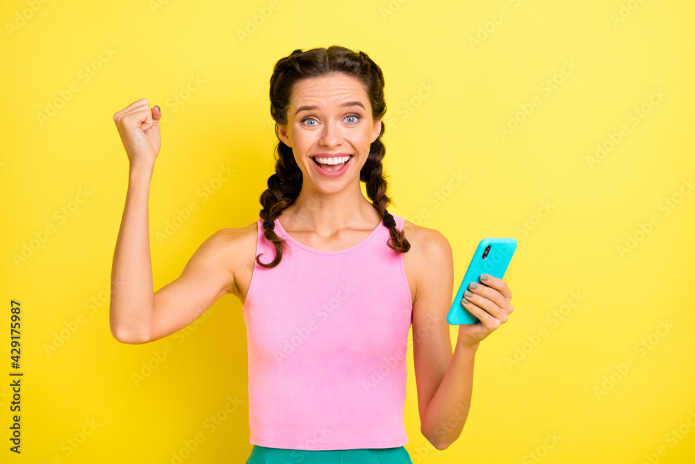 Photo of celebrating young lady braids dressed singlet rising fist holding modern gadget isolated yellow color background