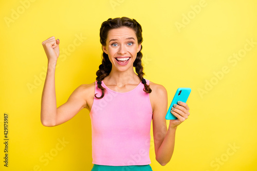 Photo of celebrating young lady braids dressed singlet rising fist holding modern gadget isolated yellow color background