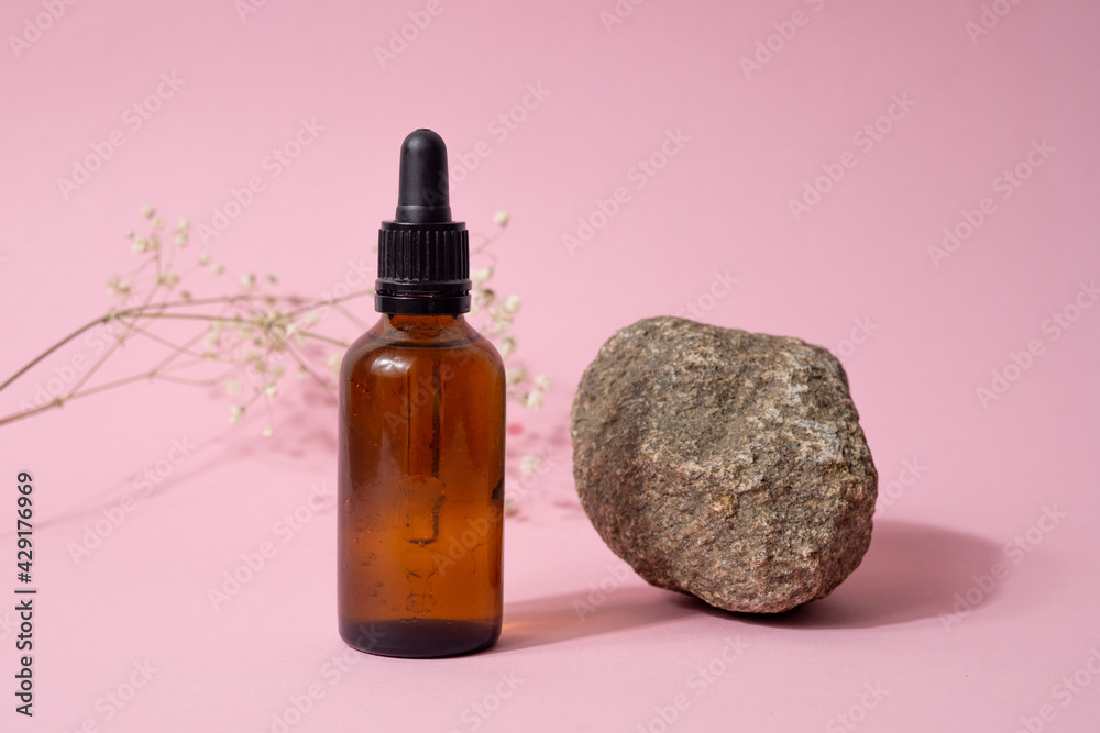 Brown glass bottle with pump of cosmetic products with dried white flower and stone on pink paper background. Natural Organic Spa Cosmetic Beauty concept Front view Brown glass bottle with pump of cosmetic products with dried white flower and stone on pink paper background. Natural Organic Spa Cosmetic Beauty concept Front view