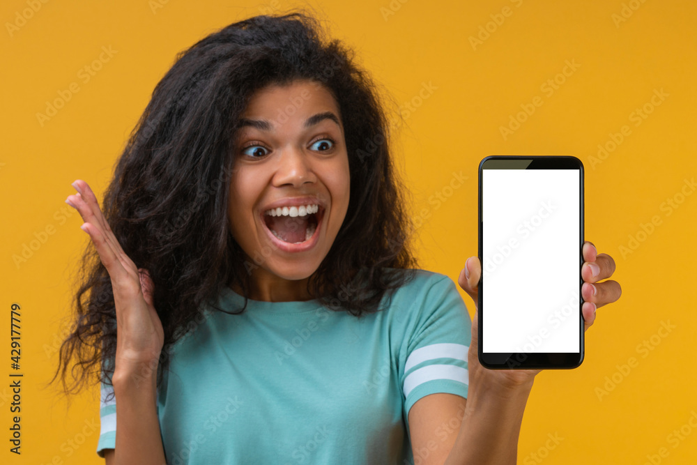 Close up portrait of euphoric dark skinned girl looking happy and shocked, showing mobile phone with blank white screen at the camera Close up portrait of euphoric dark skinned girl looking happy and shocked, showing mobile phone with blank white screen at the camera