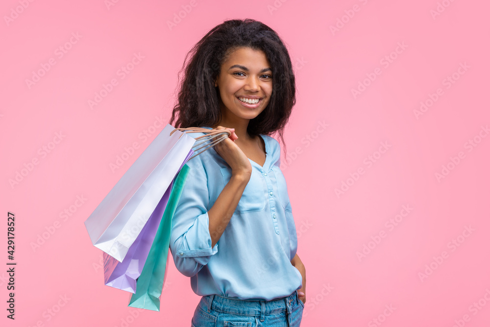 Studio shot of beautiful stylish african girl with a perfect smile posing with piles of paper shopping bags in hands isolated over vivid orange yellow background Studio shot of beautiful stylish african girl with a perfect smile posing with piles of paper shopping bags in hands isolated over vivid orange yellow background