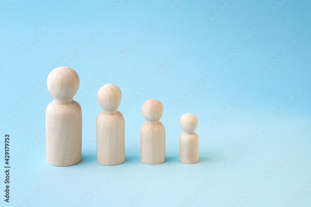 Wooden figurines standing in line from high to low on blue background. Family members or personal degradation concept Wooden figurines standing in line from high to low on blue background. Family members or personal degradation concept