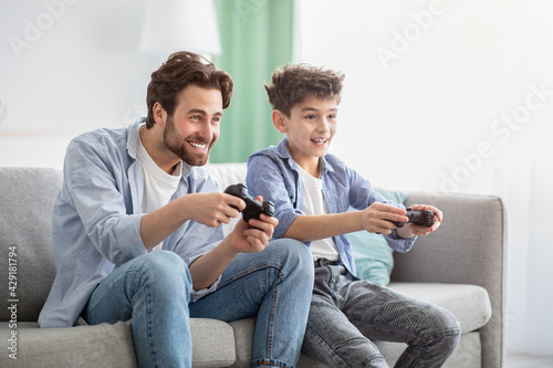 Boys are boys. Joyful father and teen son competing with each other in online video games, using joysticks