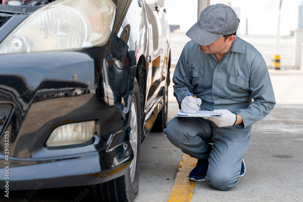 A Young Mechanic Writing On Clipboard Examining Car Wheel A Young Mechanic Writing On Clipboard Examining Car Wheel