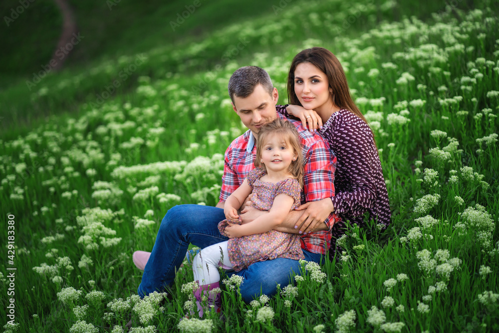 Fototapeta premium young family is sitting on the green grass. flowers bloom around