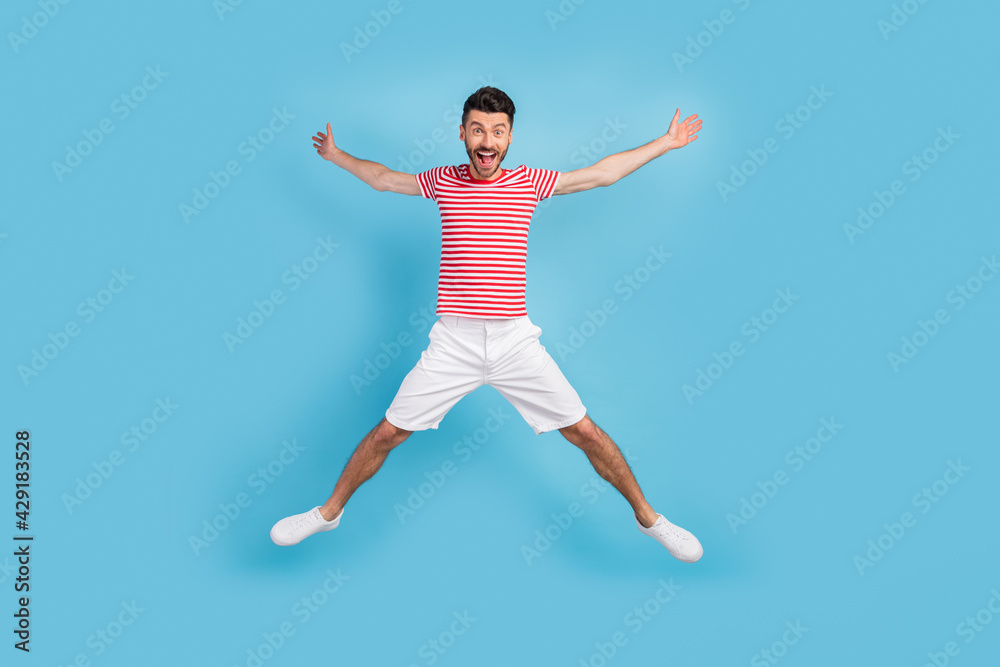 Full length photo of cute funky young man dressed striped t-shirt jumping high like star isolated blue color background