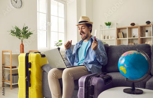 Obraz na plátně Happy man traveler sitting on home sofa with packed luggage suitcase rejoice suc