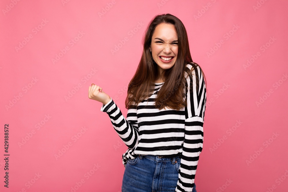 Portrait of young positive happy attractive brunette woman with sincere emotions in casual striped pullover isolated on pink background with free space and celebrating winning shouting yeah Portrait of young positive happy attractive brunette woman with sincere emotions in casual striped pullover isolated on pink background with free space and celebrating winning shouting yeah