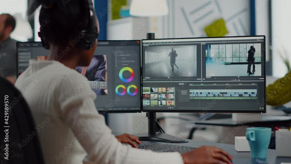 African video editor working with footage and sound, editing new project cutting film montage sitting in modern agency office. Woman using computer processing movie in post production software