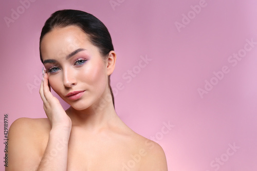 Portrait of young beautiful woman with perfectly clean face skin wearing professional make up touching her face. Female with long black hair tied in a ponytail. Close up, copy space, background.