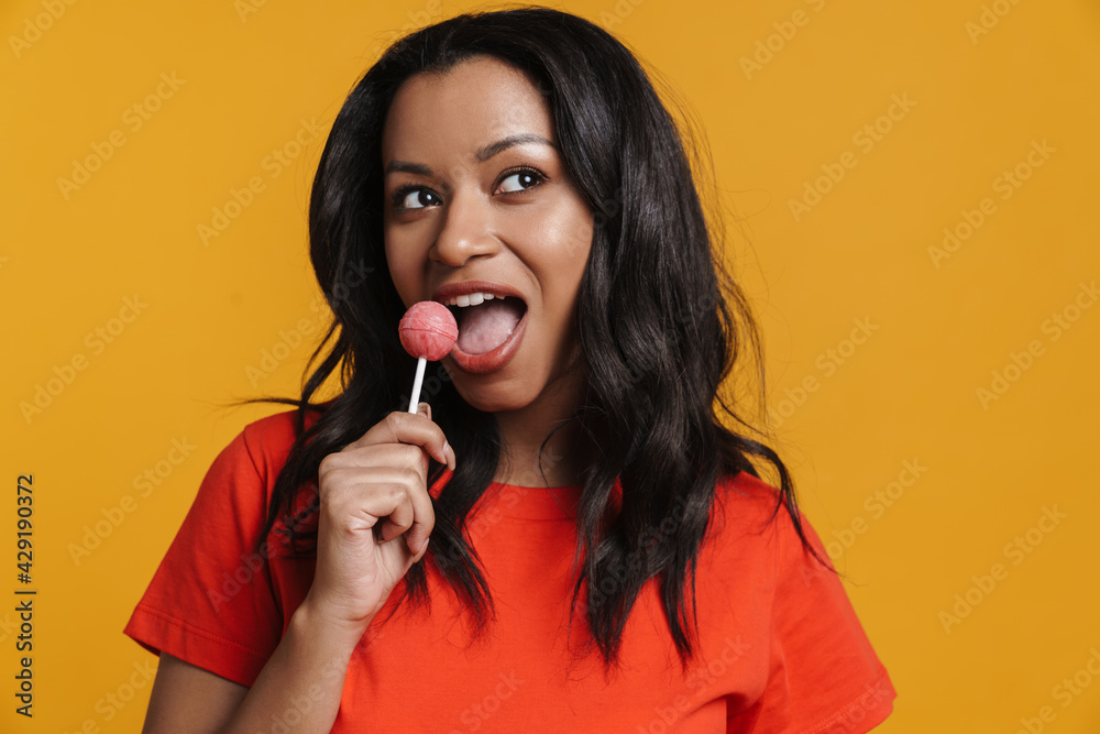 Young black woman smiling while licking lollipop Young black woman smiling while licking lollipop
