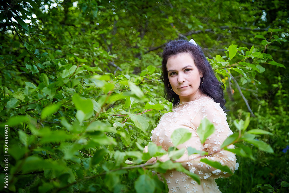 Young beautiful female model in pink dress posing in the summer park or garden with greenery arround her. Girl walking in a forest. Young beautiful female model in pink dress posing in the summer park or garden with greenery arround her. Girl walking in a forest.