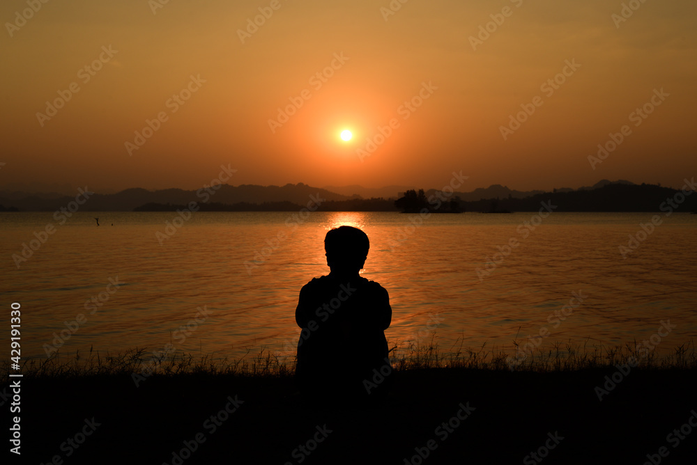 silhouette of a man who sitting beside huge lake and looking the sunset view