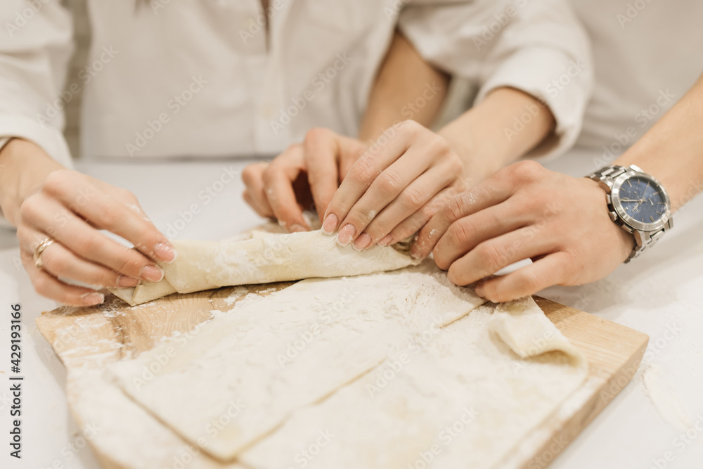 Male and female hands roll out the dough with a rolling pin and flour Male and female hands roll out the dough with a rolling pin and flour