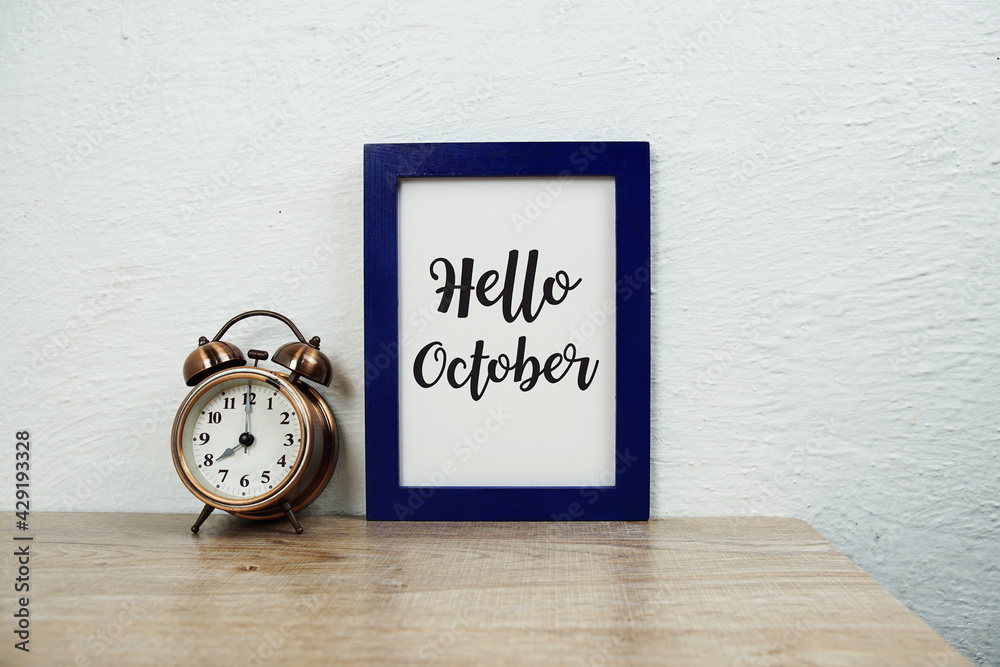 Hello October typography text and alarm clock on wooden table background Hello October typography text and alarm clock on wooden table background