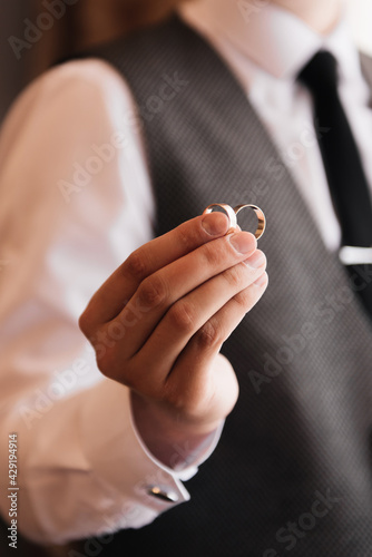 The groom holds 2 wedding rings in his hands