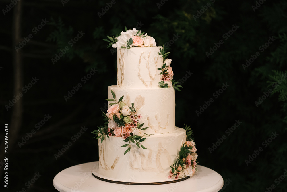 Luxury wedding tiered white cake decorated with flowers, photo at night on the background of lights